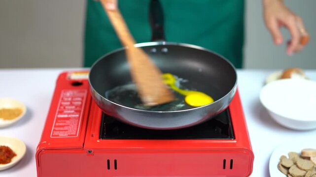 Close up of hands cracking and scrambling an egg in a black frying pan