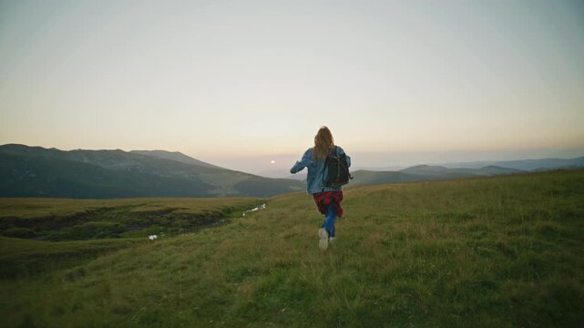 Person enjoys sunset on a grassy hillside with hands raised wide in the air as sunlight fades behind the mountains at dusk
