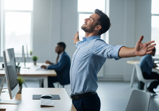 Happy young man stretching arms after finishing work on laptop at home office.