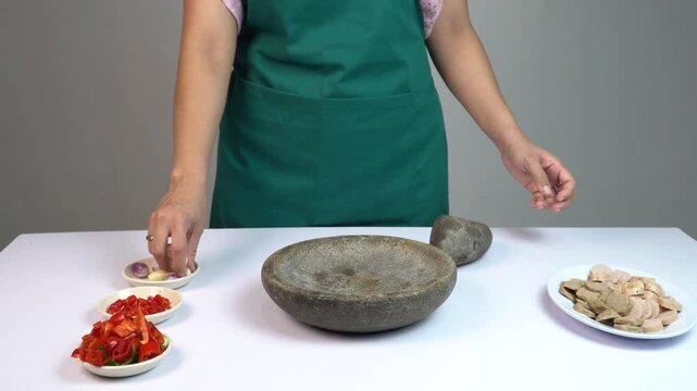 Female chef in green apron crushing garlic with traditional stone mortar and pestle