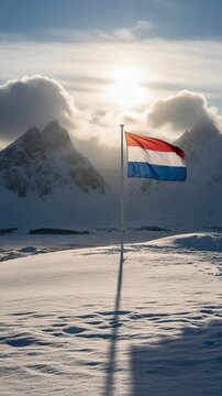 Dutch flag waving in snowy mountain landscape with dramatic winter sun and snow-covered peaks background
