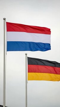 Flags of the Netherlands and Germany waving proudly on flagpoles against a cloudy sky, representing international cooperation, diplomacy, and European unity.