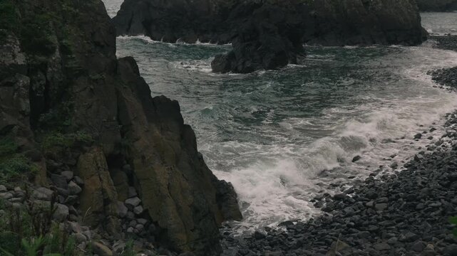Waves crashing onto a beach beneath steep coastal cliffs