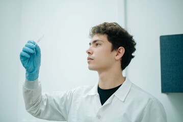 Young male scientist holding a small laboratory vial up to the light, carefully examining its contents during a scientific research procedure. © LuisPimenttel