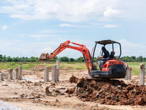 Compact track backhoe machine digging soil and clearing land for building foundation development in a rural outdoor field.
