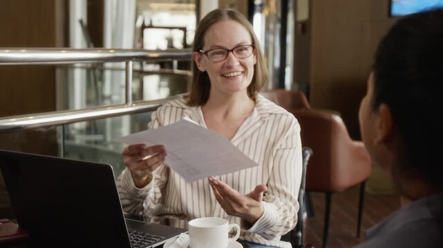 Caucasian woman with disability in wheelchair receiving document from Latin colleague during business meeting in cafe. Clip is ideal for corporate diversity and inclusion campaigns