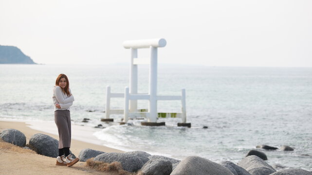 Japan: A woman looks toward the iconic white torii gate standing in the sea on Itoshima's serene coastline.