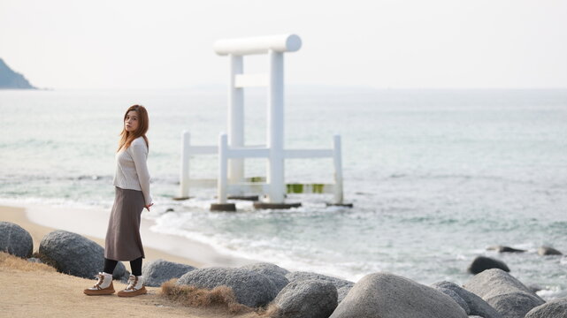 Japan: A woman looks toward the iconic white torii gate standing in the sea on Itoshima's serene coastline.