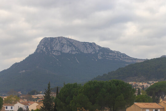 Toulon, France &ndash; December 31, 2025: The prominent limestone massif of Mont Faron rises above the village, with summit communication towers visible under a cloudy sky.