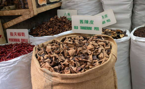 White sacks filled with dried spices, peppercorns, and chillies are displayed with bilingual labels at a market stall.