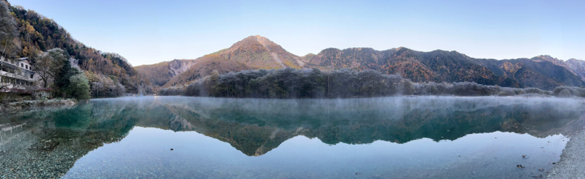 Morning mist lingers over the perfect reflection of Mount Yake on Taisho Pond's mirror-like water.