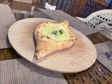 Khachapuri - A traditional boat-shaped cheese bread topped with fresh dill rests on a wooden plate.