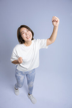 [ブルー背景]笑顔でガッツポーズで腕を高く伸ばして運動する女性、ダイエット成功や健康的で前向きな40代のミドル世代のフィットネスイメージ