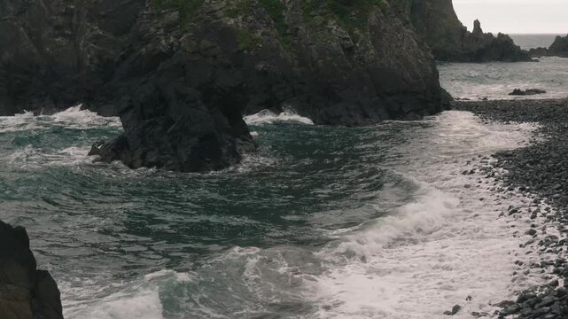 Waves crashing onto a beach beneath steep coastal cliffs