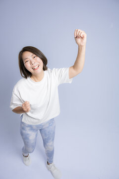 [ブルー背景]笑顔でガッツポーズで腕を高く伸ばして運動する女性、ダイエット成功や健康的で前向きな40代のミドル世代のフィットネスイメージカメラ目線