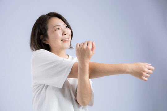 [Blue Background] A woman in her 40s smiling as she stretches to stay healthy during menopause; fitness exercises to loosen up before working out