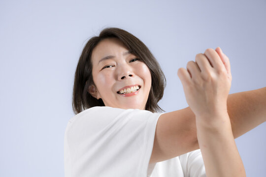 [ブルー背景]更年期も健康のために笑顔でストレッチする40代女性、運動前に体をほぐすのフィットネス　カメラ目線
