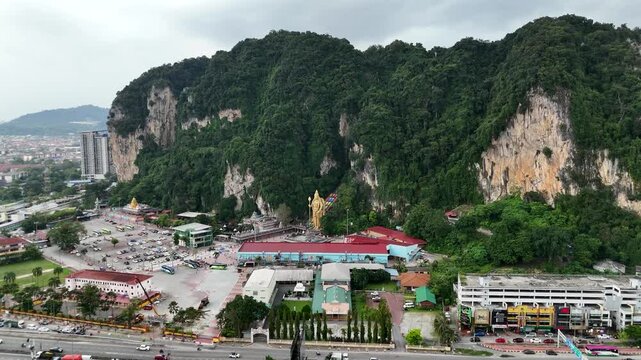 Aerial landscape shot revealing massive limestone mountains as drone smoothly approaching the famous Batu Caves landmark under cloudy sky