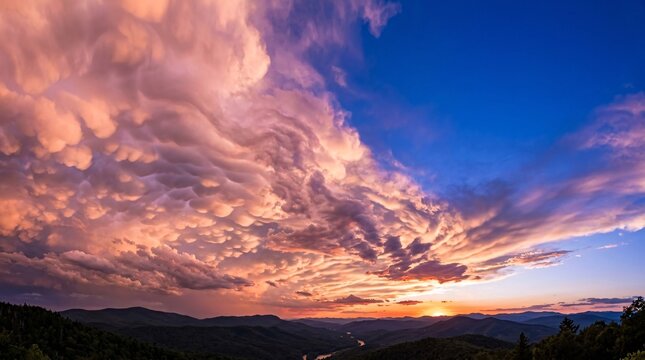 Spectacular colorful sunset sky with dramatic pink and purple clouds over dark rolling mountain silhouettes.