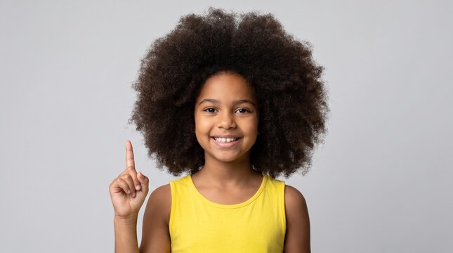 Happy young girl with large afro hair smiling and pointing finger up toward a creative idea or inspiration
