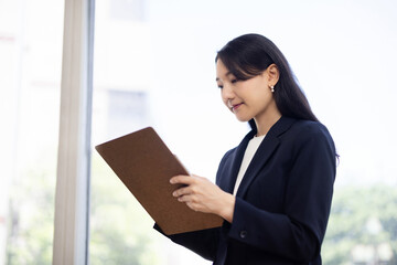 Fototapeta premium Young Japanese businesswoman taking notes on a clipboard by a bright window
