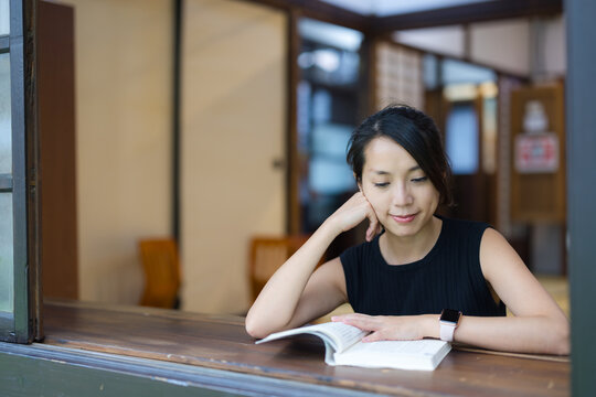 Woman sitting at a wooden table indoors and reading a book