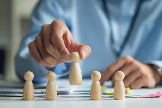 Close-up of worker hand picking or selecting wooden doll for human resources recruitment and hiring concept.