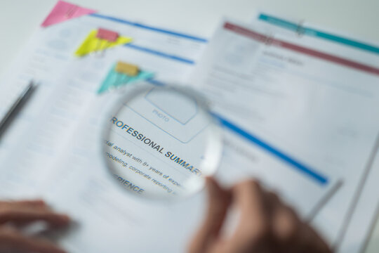 Close-up of magnifying glass focusing on words of resume document for recruitment concept.