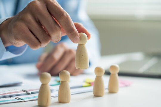 Close-up of worker hand picking or selecting wooden doll for human resources recruitment and hiring concept.