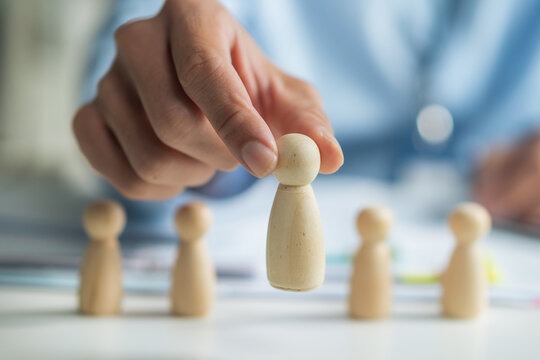 Close-up of worker hand picking or selecting wooden doll for human resources recruitment and hiring concept.
