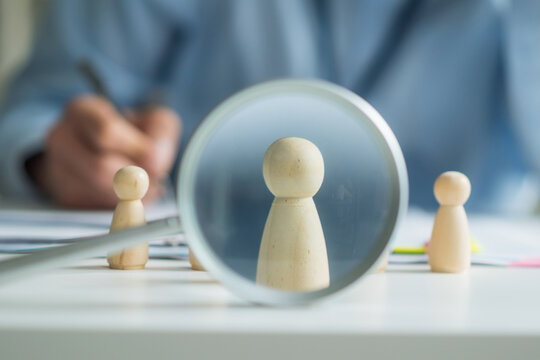 Close-up of magnifying glass focusing on wooden doll for human resources recruitment and hiring concept.