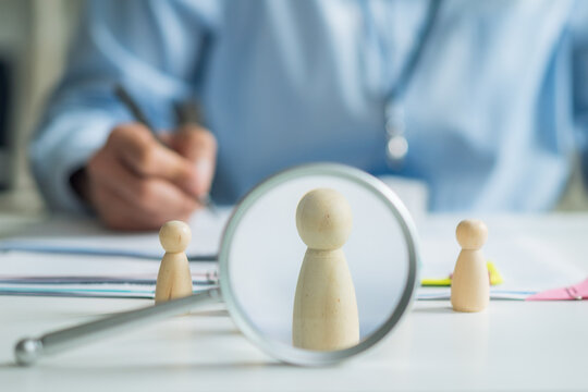 Close-up of magnifying glass focusing on wooden doll for human resources recruitment and hiring concept.