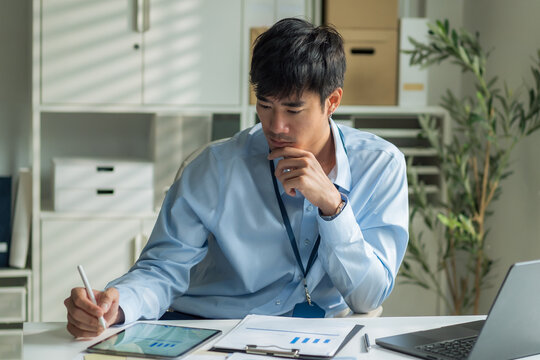 Office worker using stylus pen on digital tablet and holding chin thoughtfully at desk.