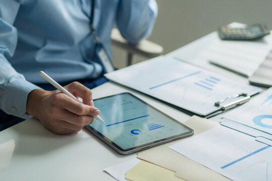 Close-up of worker holding stylus pen writing on digital tablet screen to check financial report at desk.