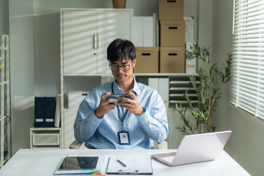 Office worker wearing glasses smiling confidently while holding smartphone at desk.