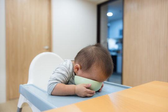 Toddler boy leaning over to eat directly from bowl on high chair tray