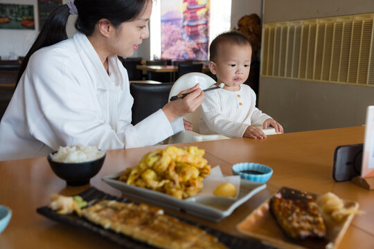 Woman feeding a toddler at a restaurant table with dishes in Taiwan