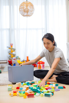Woman sitting on a living room floor packing toys into a storage container