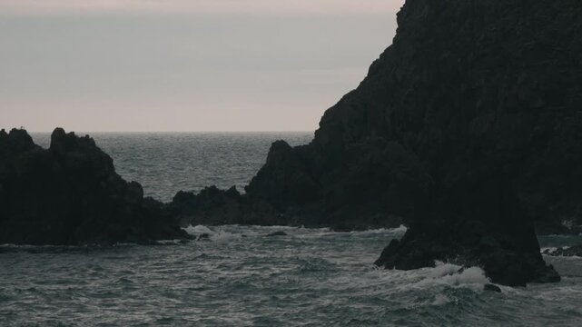 Waves crashing onto a beach beneath steep coastal cliffs