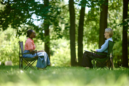 Young adult African American woman talking with senior Caucasian female therapist in park, representing outdoor psychotherapy session, perfect for mental health marketing