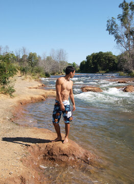 Young Man Standing On River Bank In Swimming Trunks No Shirt