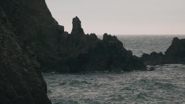 Waves crashing onto a beach beneath steep coastal cliffs
