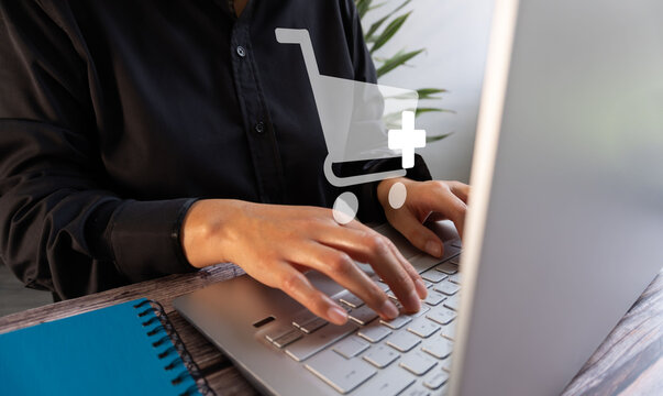 Person types on laptop with shopping cart icon overlayed. Hands focused, suggesting online shopping or e-commerce activity. Suitable for web design