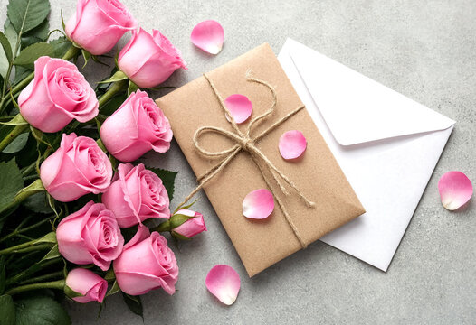 Beautiful pink roses with rose petals and a wrapped gift package on grey surface