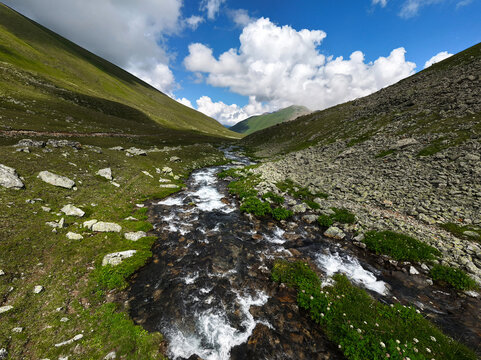 Mountain Stream Flowing Through Alpine Valley Under Cloudy Sky