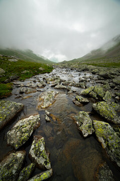 Rocky mountain stream flowing through alpine valley under foggy sky