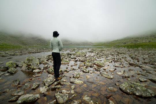 Female Hiker standing among rocks in a misty lake landscape