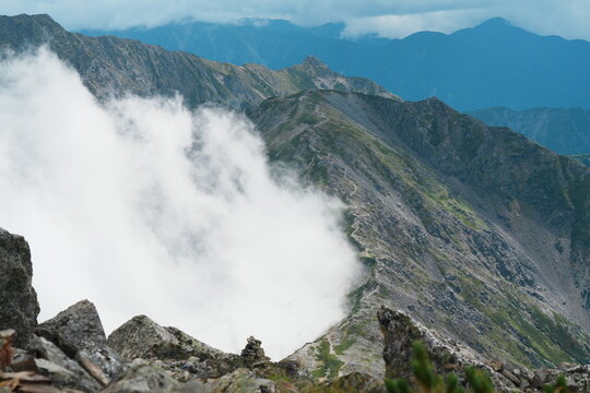 夏の北岳で稜線を越えて這い上がる雲と尾根をたどる登山道の細い筋