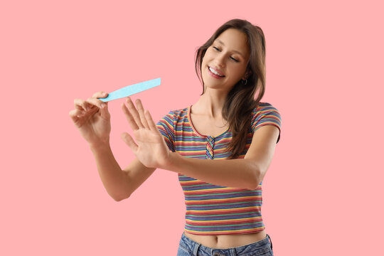 Self care and beauty routine, young woman filing fingernails with a nail file for manicure and grooming on a solid pink background