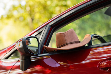 Road trip and travel adventure, brown cowboy hat resting on the open window of a red car during a...